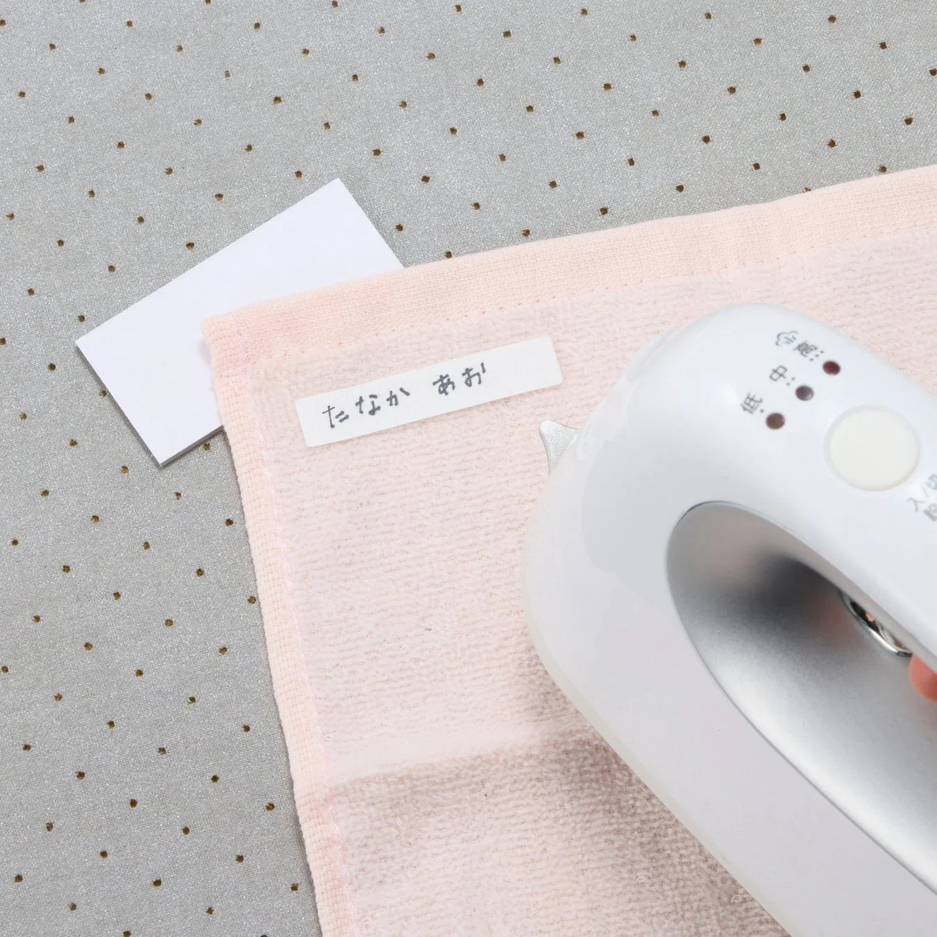 ピンクのタオルにネームタグをアイロンで貼り付けている様子