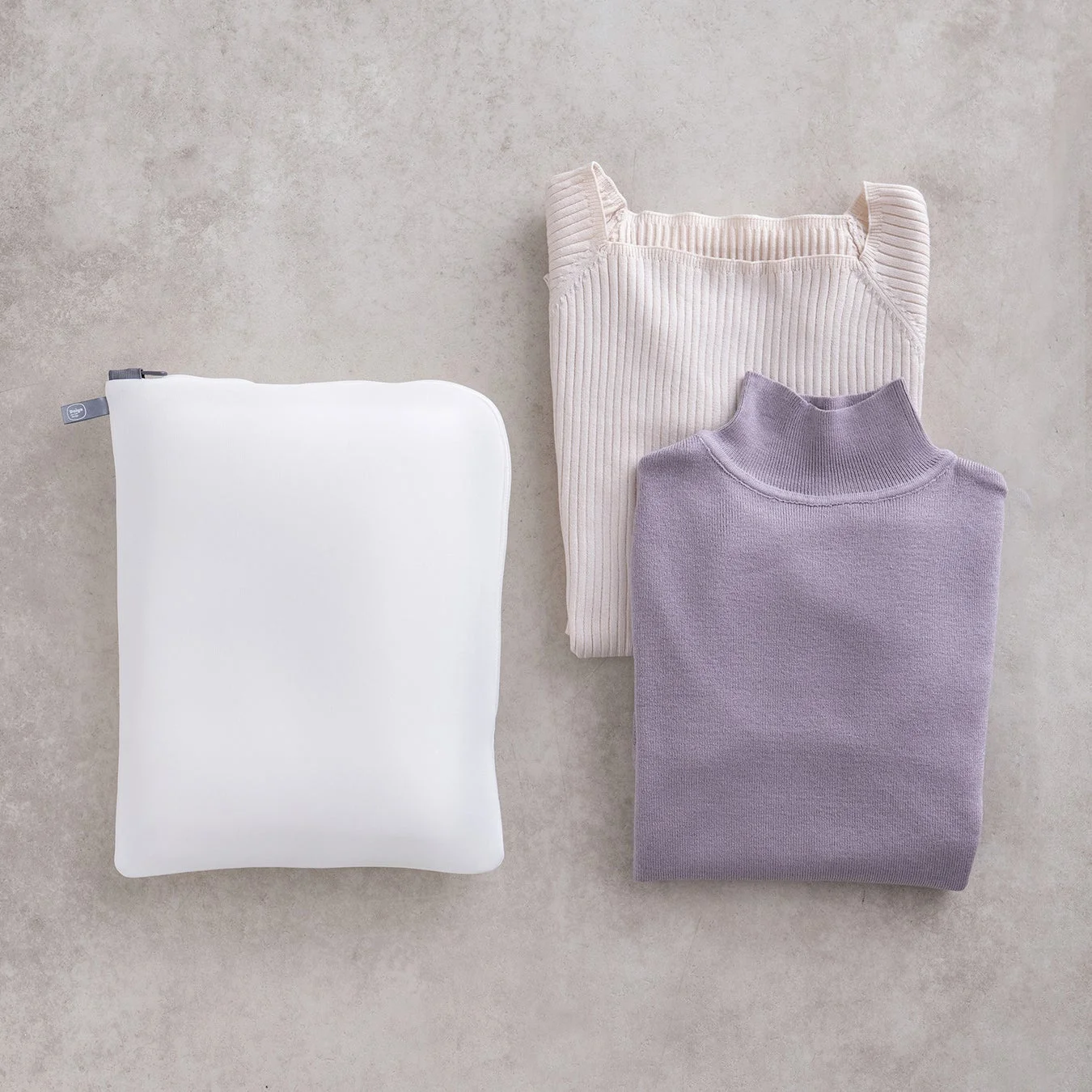 白い衣類収納ポーチと、オフホワイトとラベンダー色のセーターが並べられています