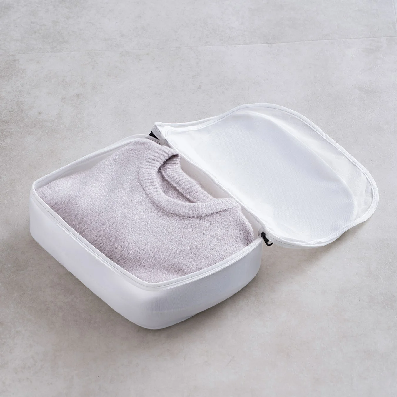 白いトラベルオーガナイザーにきれいにたたまれた薄紫色のセーターが収納されている様子