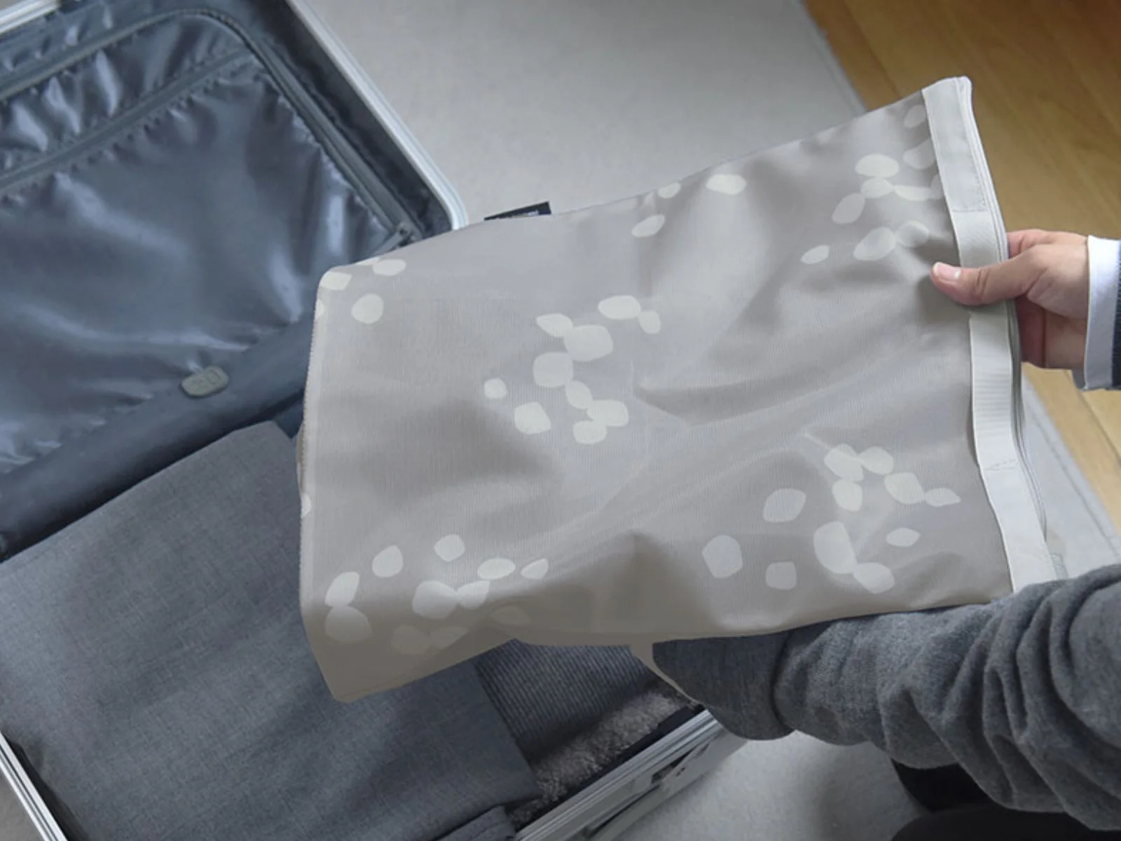 開いたスーツケースに、水玉模様の収納ポーチとたたまれた衣類を詰めている様子。旅行の準備や荷造りの場面を表しています。